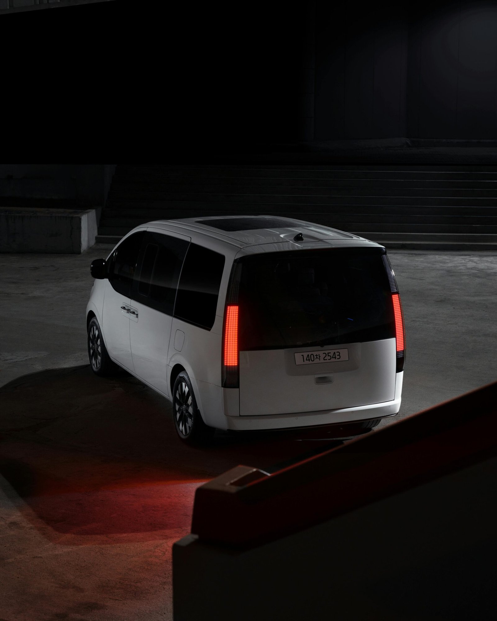 A sleek white Hyundai Staria captured in a dimly lit urban environment at night, highlighting its modern design.